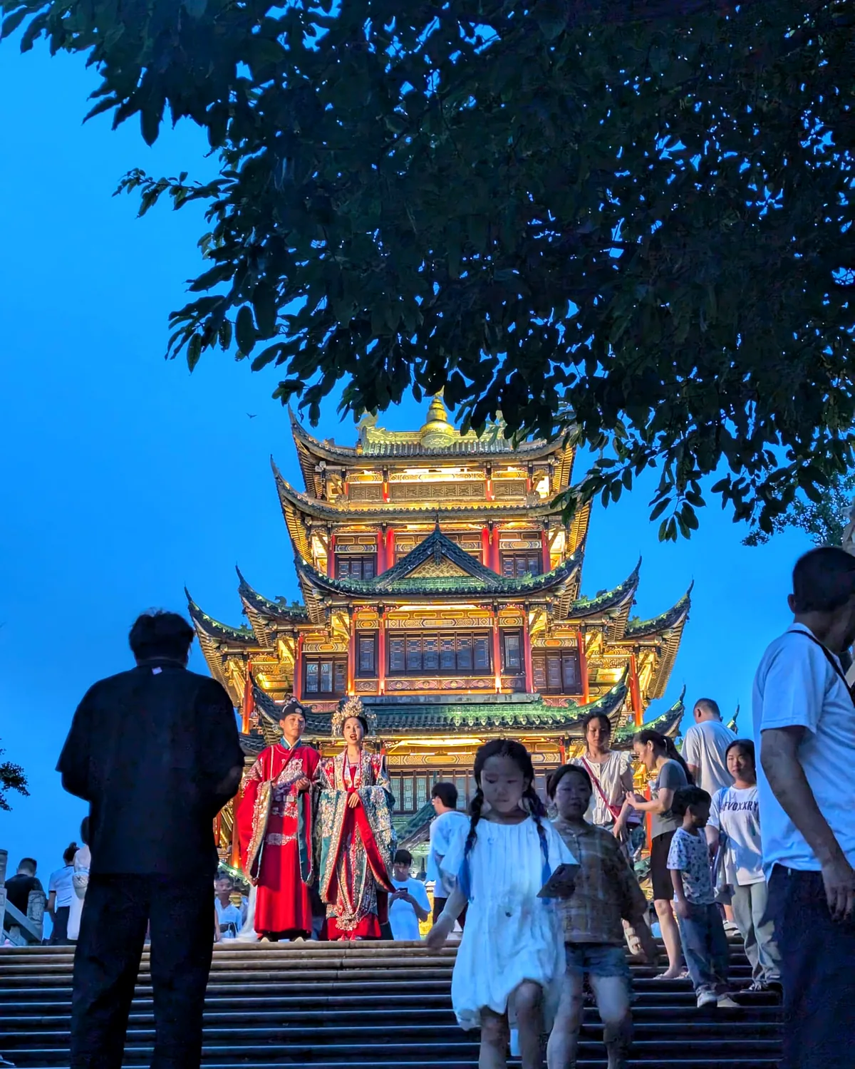 Une pagode illuminée à l'heure bleue, en haut d'un escalier plein de monde, au Hong'en Temple Forest Park de Chongqing